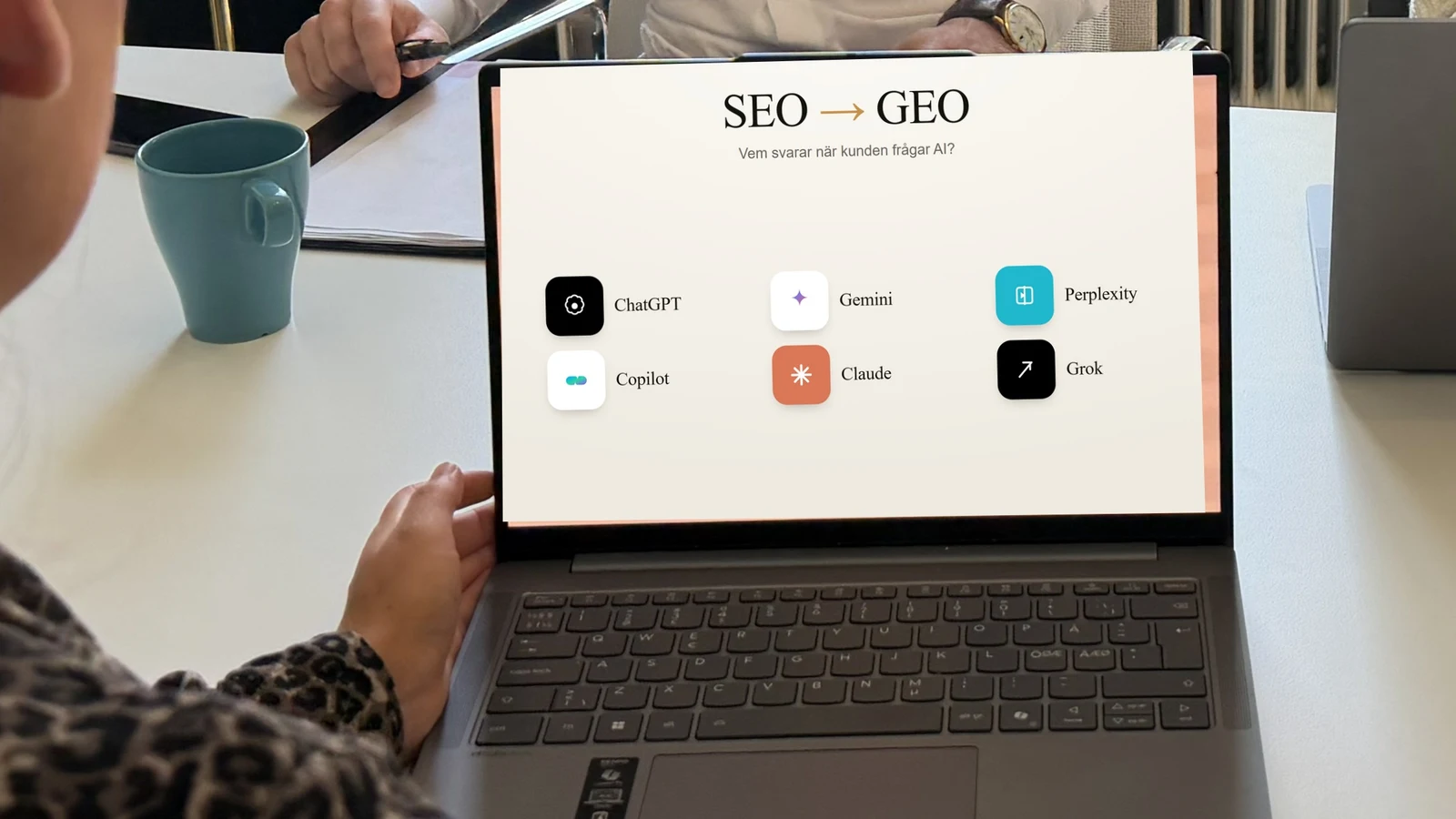 En laptop på ett kontorsbord med skärmen som visar SEO till GEO och AI-plattformarnas ikoner